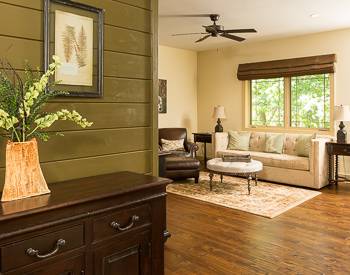 Wood floors with a leather high back chair, round table and a light colored sofa tan walls and to the left is Green wood wall